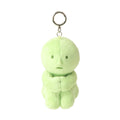 Image shows green plush SMISKI figure  with embroidery eyes and mouth is in a sitting position holding its knees. A silver loop and keychain clip is attached to its head.